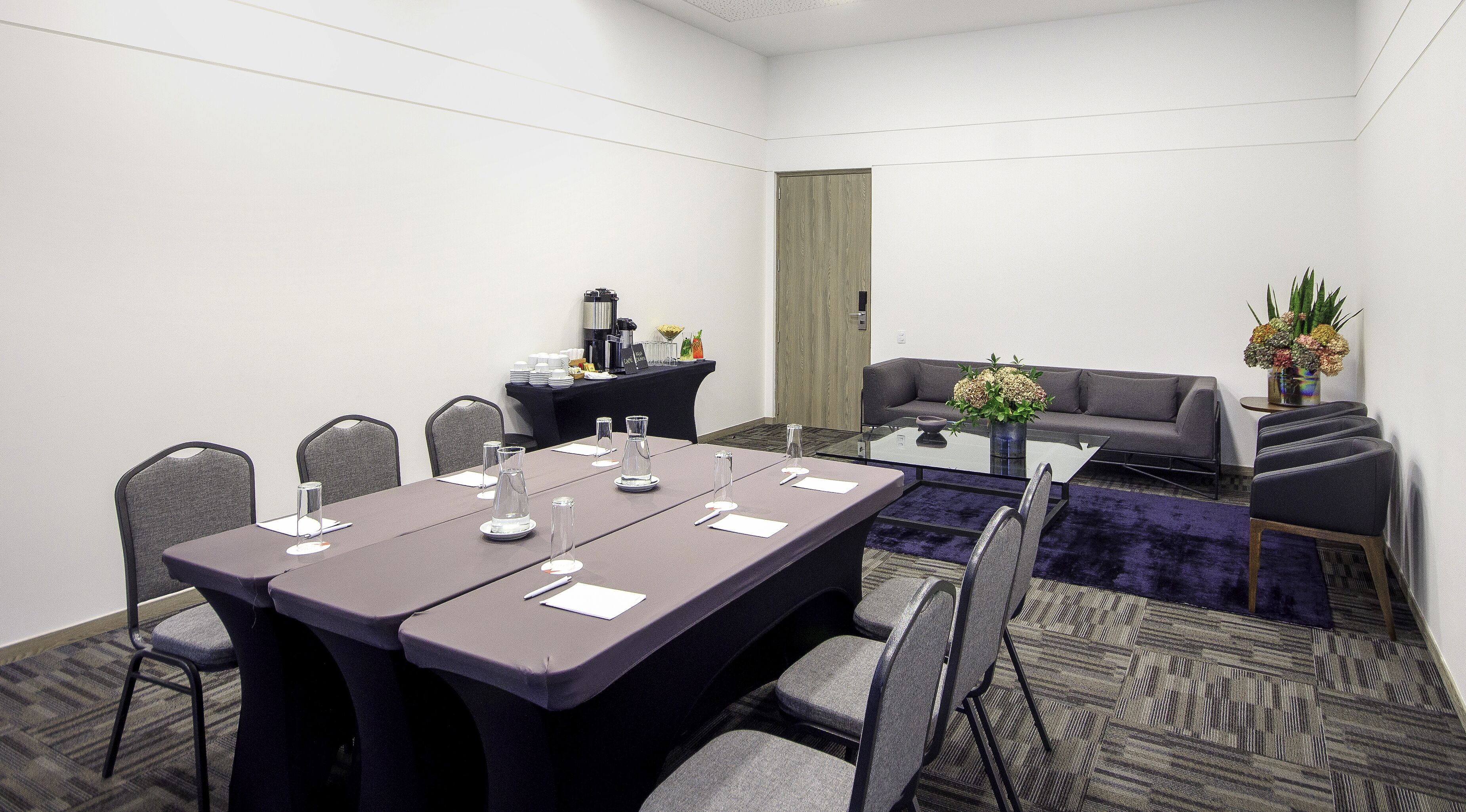 A conference room with a long table, chairs, a coffee station, and a sofa.