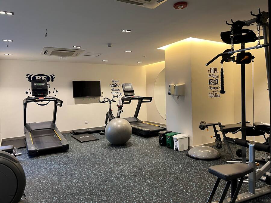 Un gimnasio con cintas de correr, una elíptica, una bicicleta estática y una pelota grande para ejercicios.