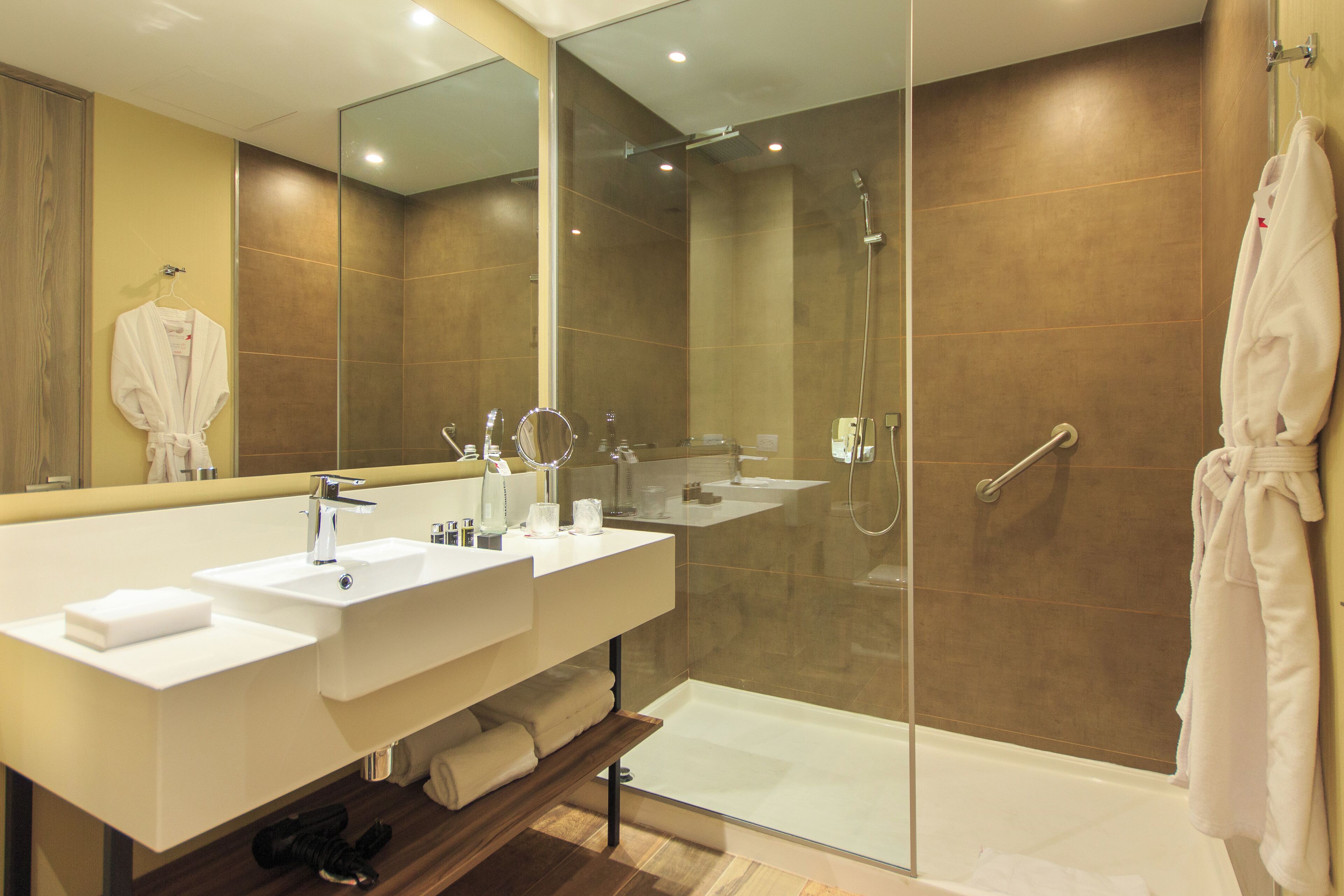 A modern bathroom with a glass-enclosed shower, a vanity with two sinks, and a large mirror.