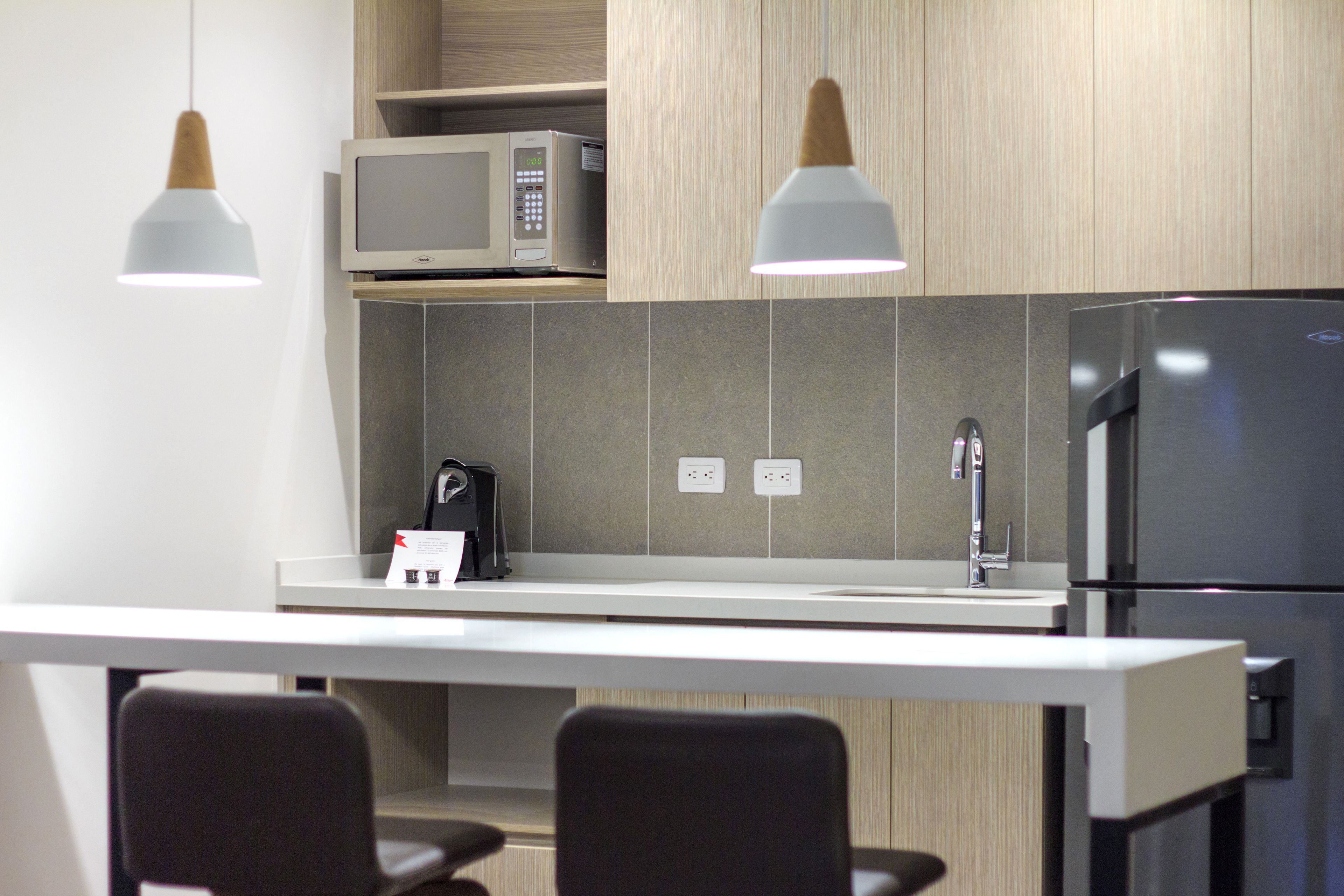 A modern kitchen with a microwave, refrigerator, and two pendant lights.