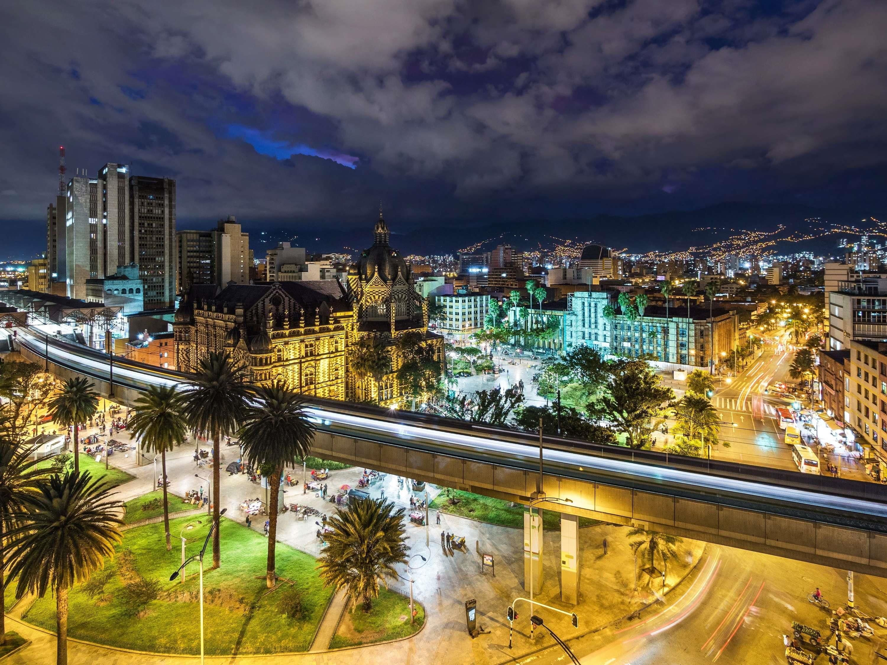 A nighttime cityscape with a prominent cathedral, a busy intersection, and a train track.