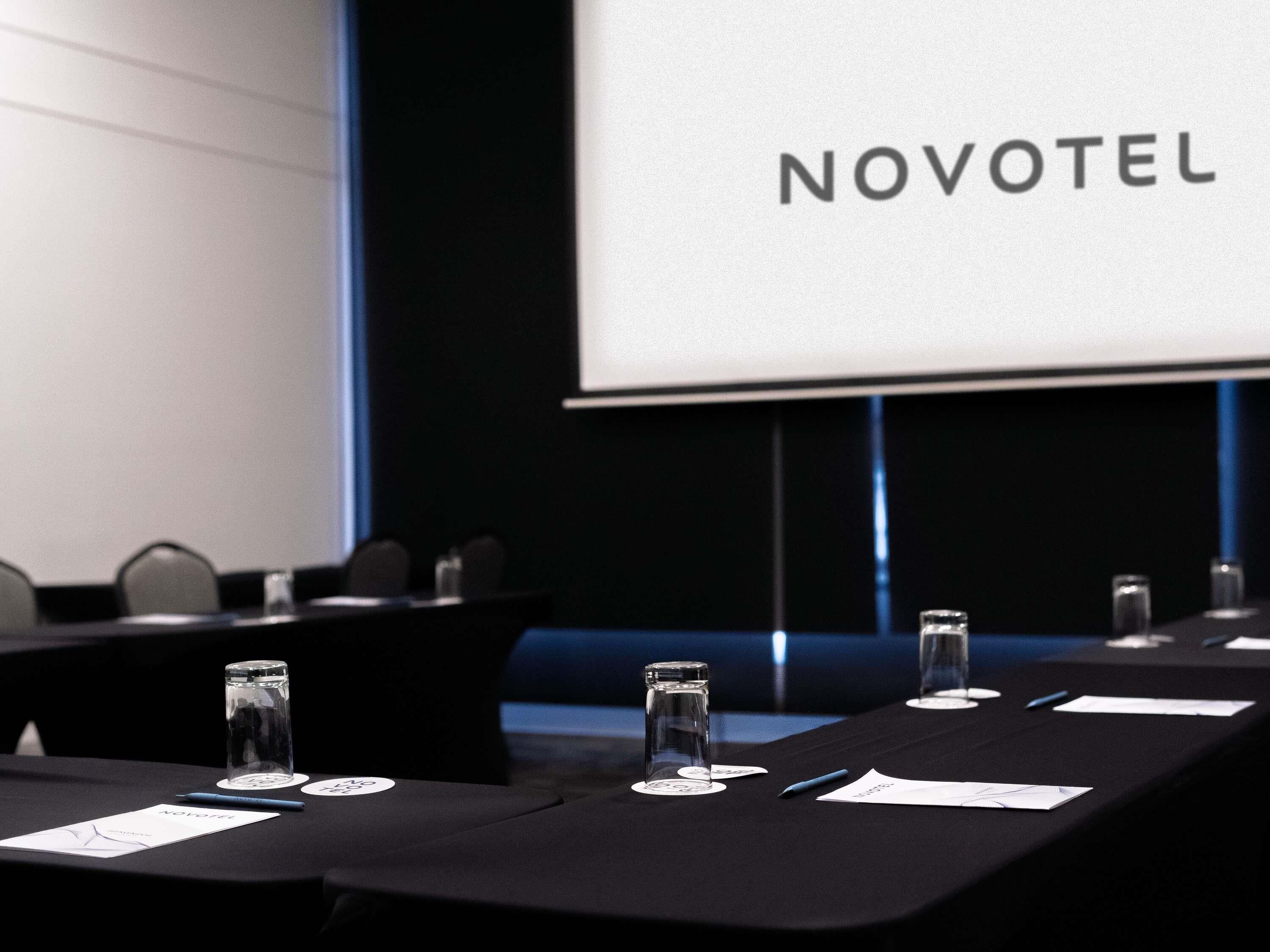 Ett konferensrum med en Novotel-skylt, namnskyltar och vattenglas på ett bord.