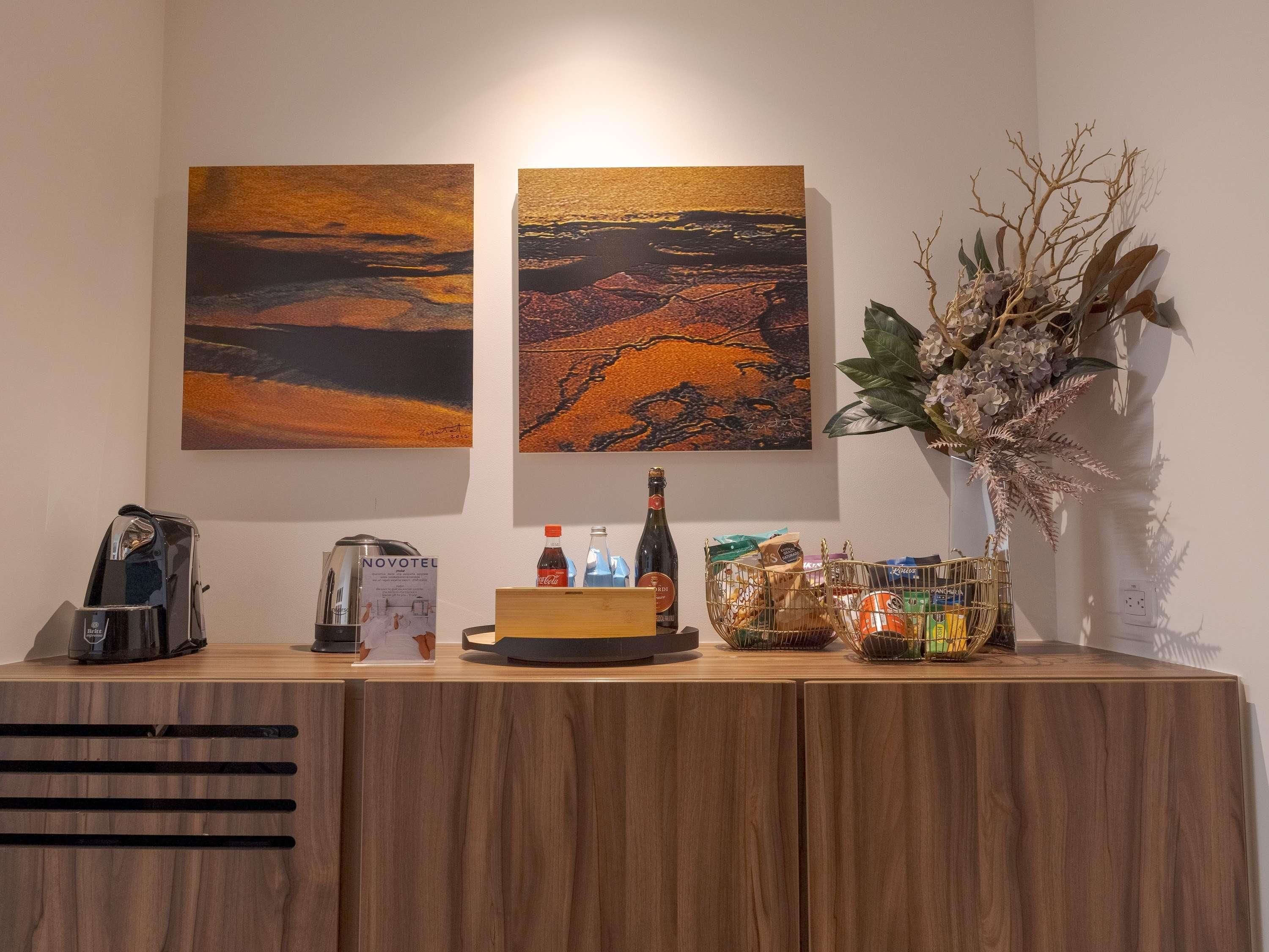 Un comptoir d’accueil en bois, avec une machine à café, un moulin à café Novotéu, une bouteille de champagne et une plante décorative.
