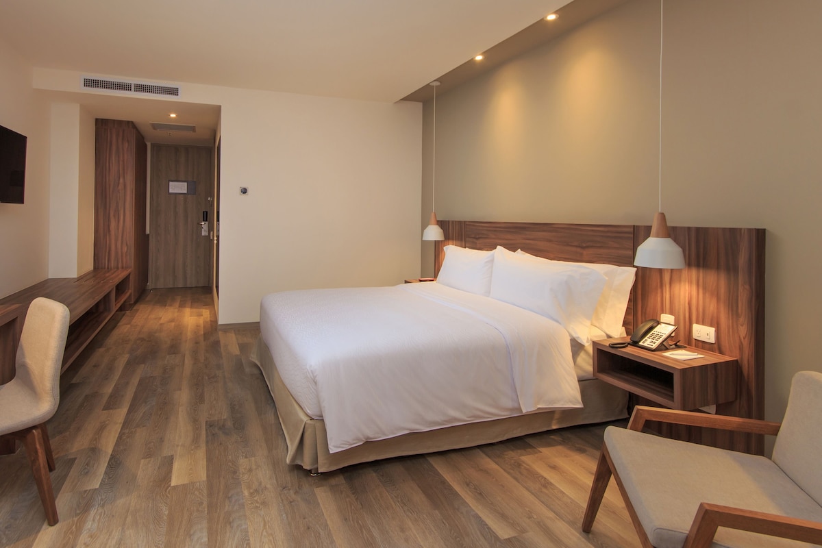 Een hotelkamer met een bed, bureau, stoelen en nachtkastje met lamp en telefoon.