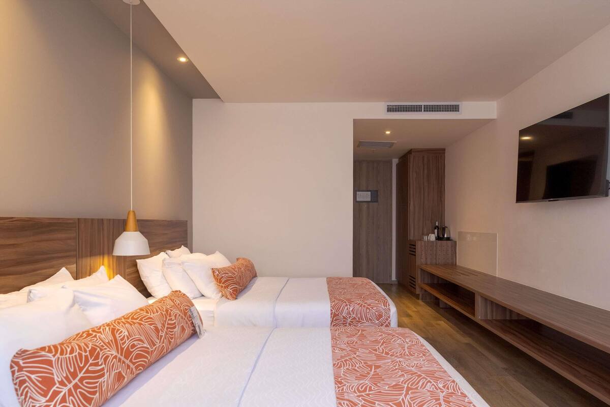 Une chambre d’hôtel avec un lit, une télévision, un banc et une tête de lit en bois.