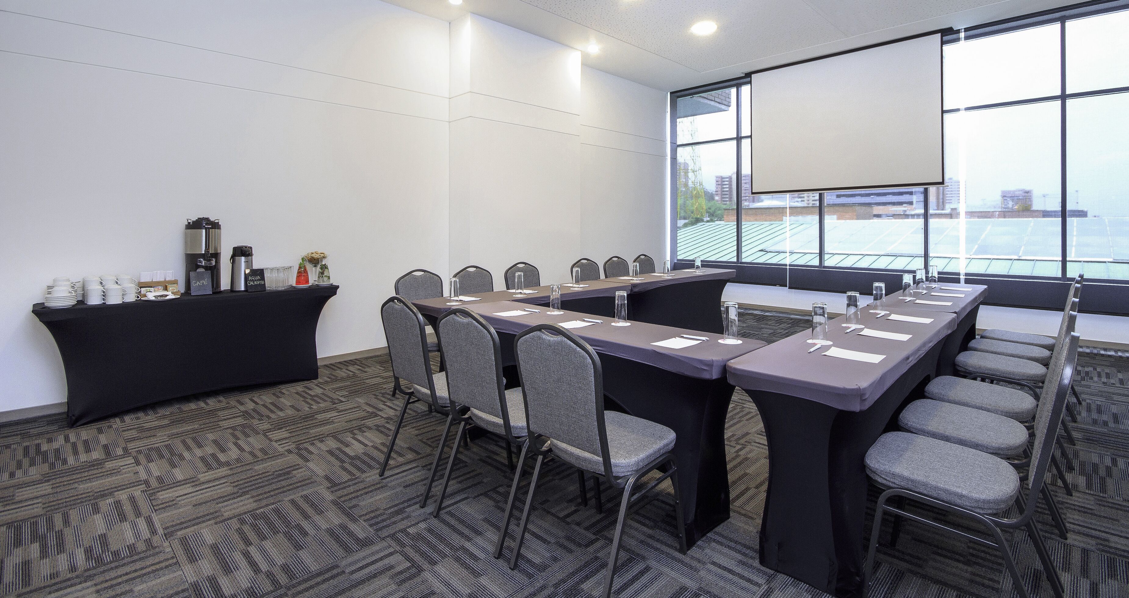 A conference room with a long table, chairs, a coffee station, and a large window with a view.
