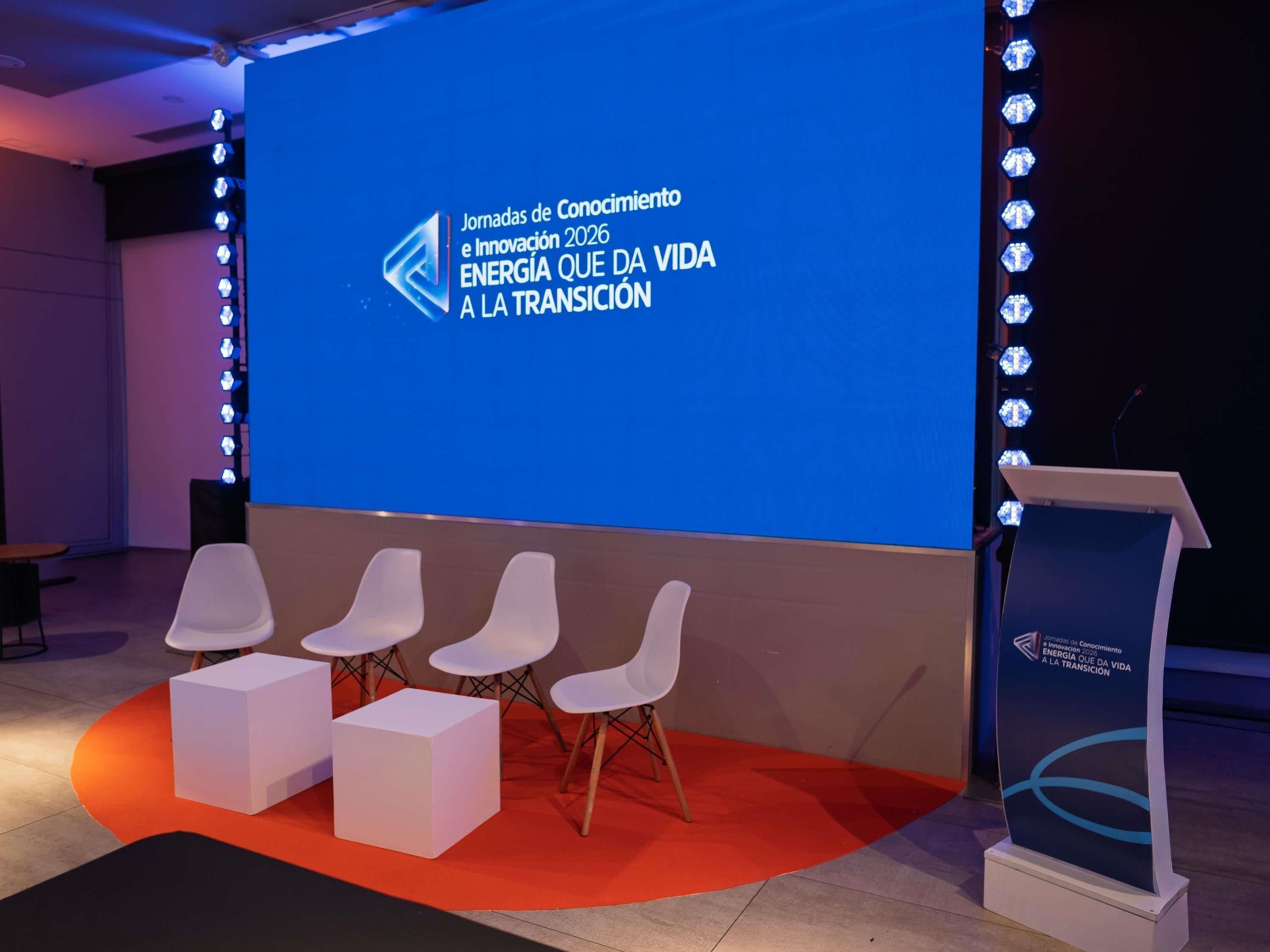 A conference room with a large screen displaying text, white chairs, and a podium.