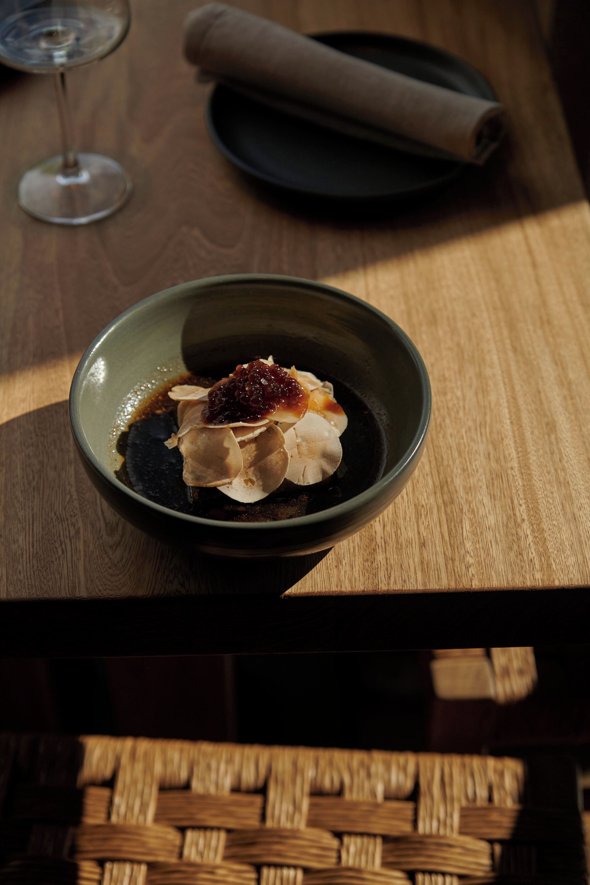A wooden table with a bowl of dessert, a glass of wine, and a rolled napkin.