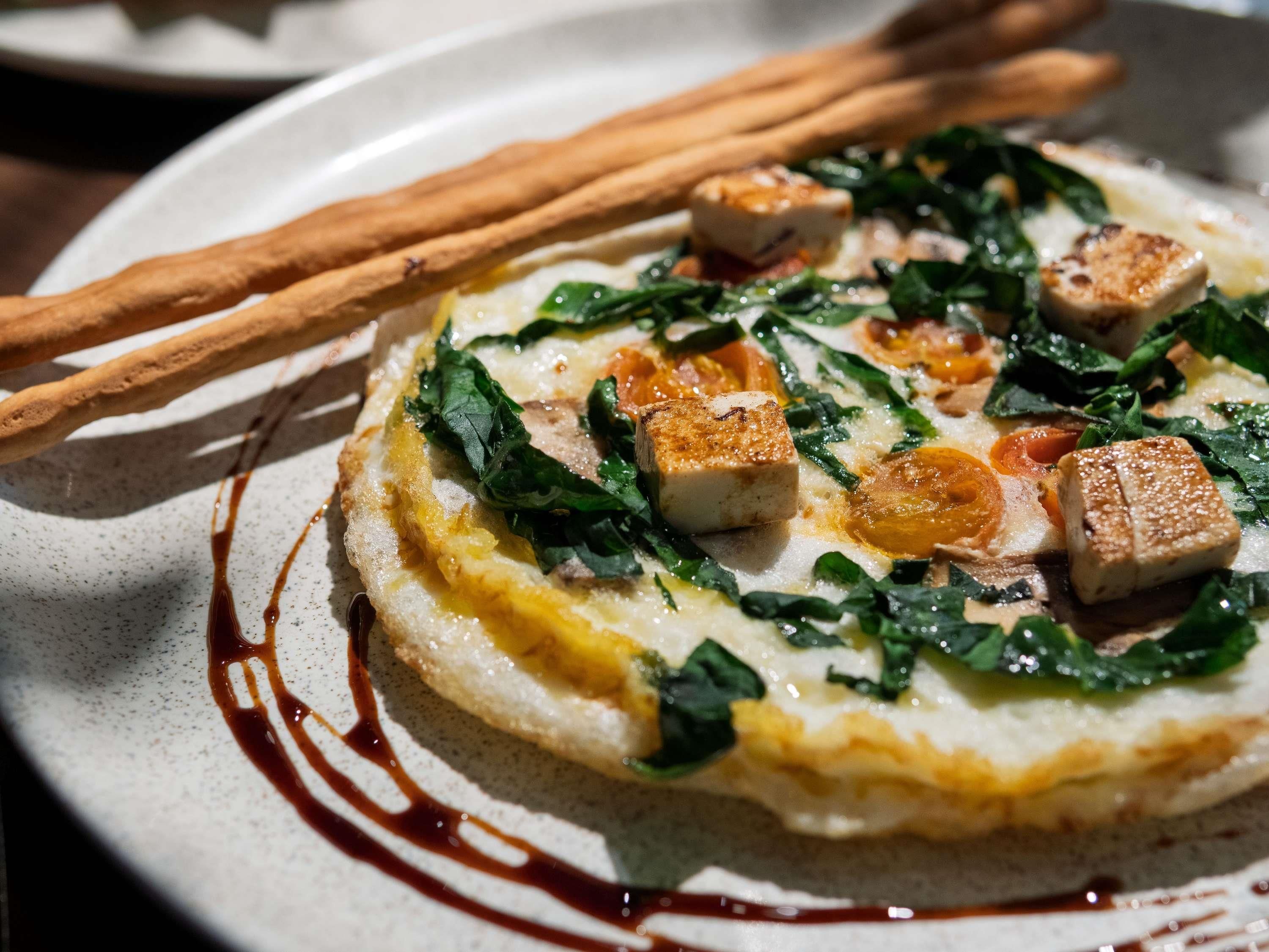 Un plato con un guiso sabroso, posiblemente una tarta o pastel, cubierto de vegetales, trozos de tofu y un chorrito de salsa.