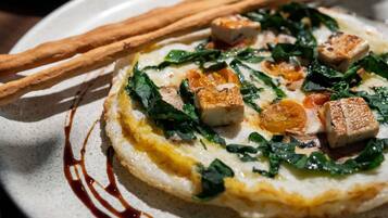 Un plato con un guiso sabroso, posiblemente una tarta o pastel, cubierto de vegetales, trozos de tofu y un chorrito de salsa.