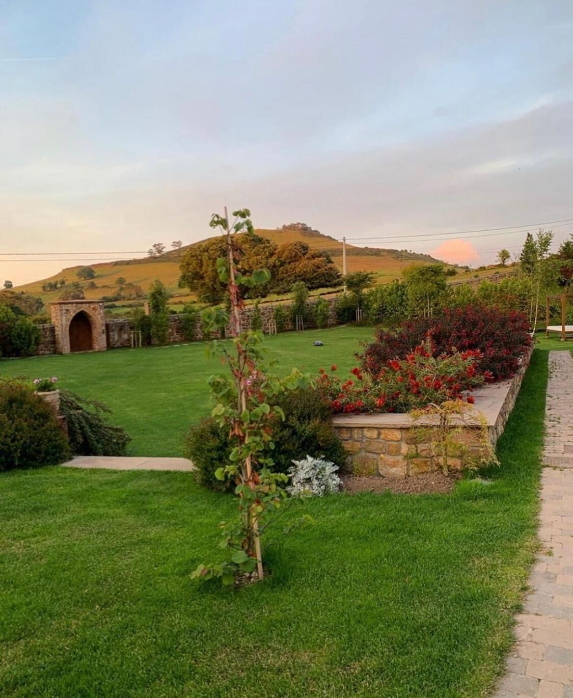 A well-maintained garden with a stone archway, a grassy lawn, and a variety of plants and flowers.