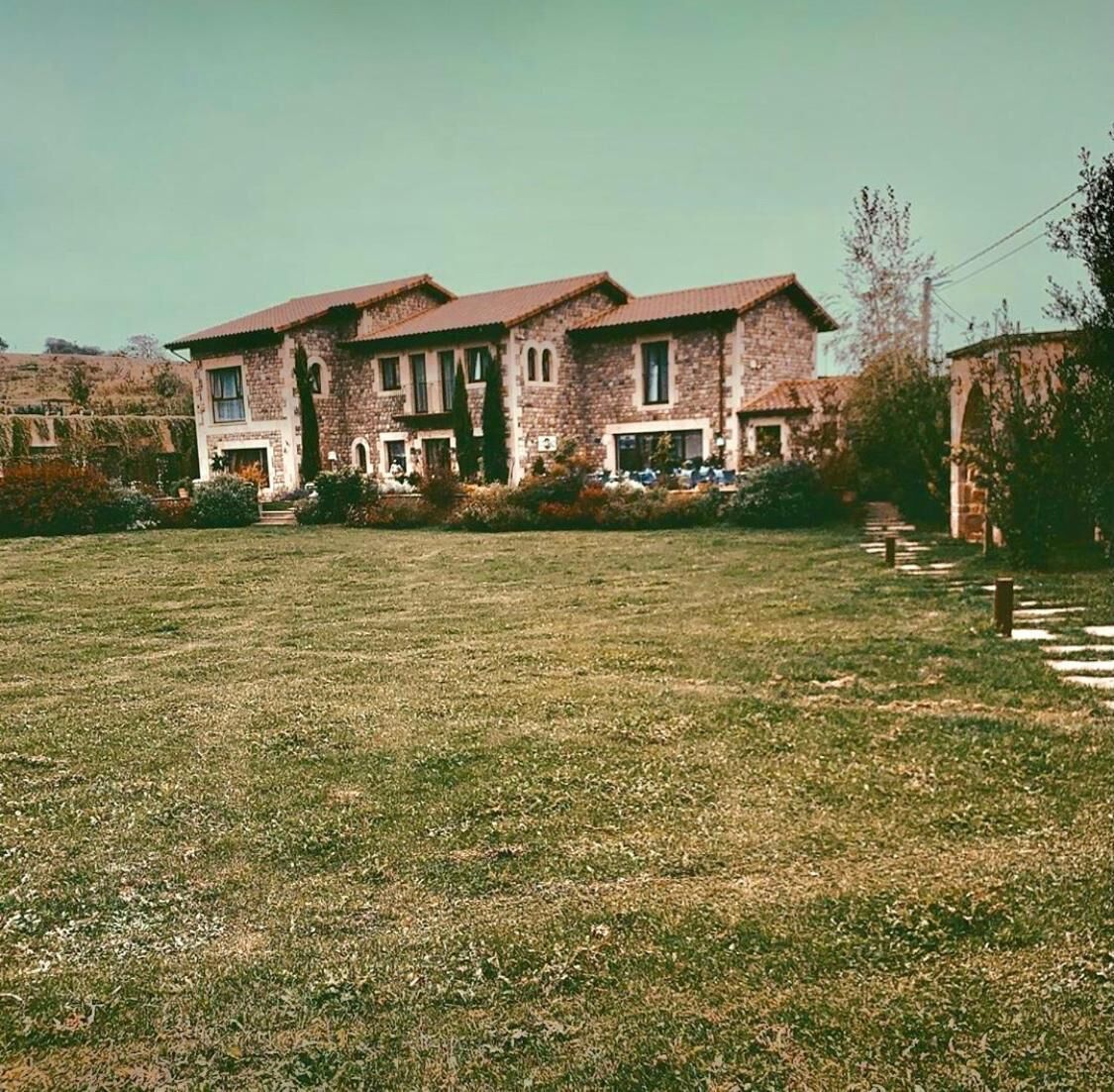 Een twee verdiepingen tellend huis met een stenen gevel, meerdere ramen en een voortuin met een pad dat naar de ingang leidt.