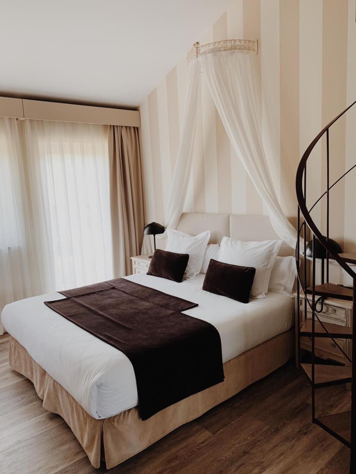 Una cama bien hecha con dosel, suelo de madera y una escalera en espiral.