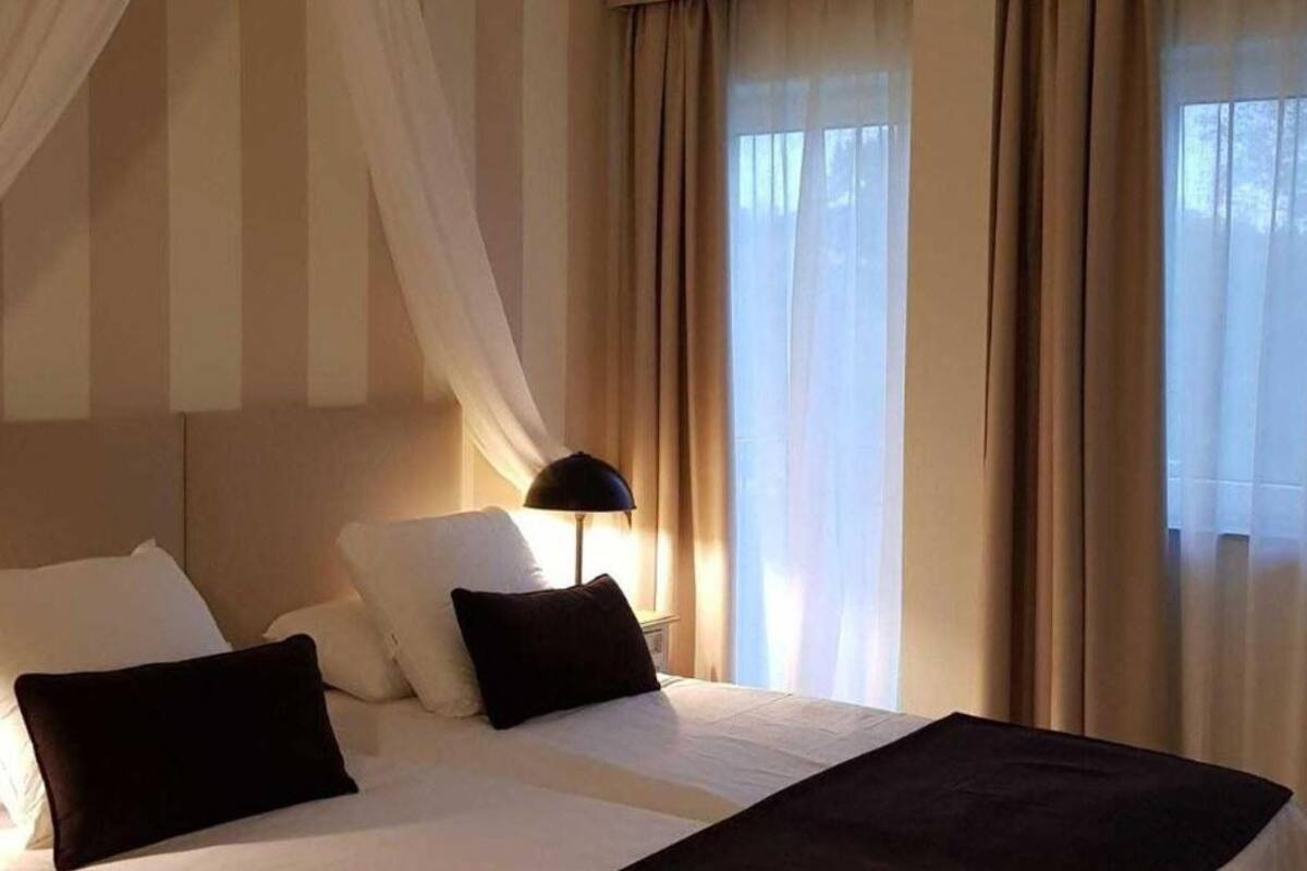 A hotel room with a bed, two pillows, a black lamp, and sheer curtains.