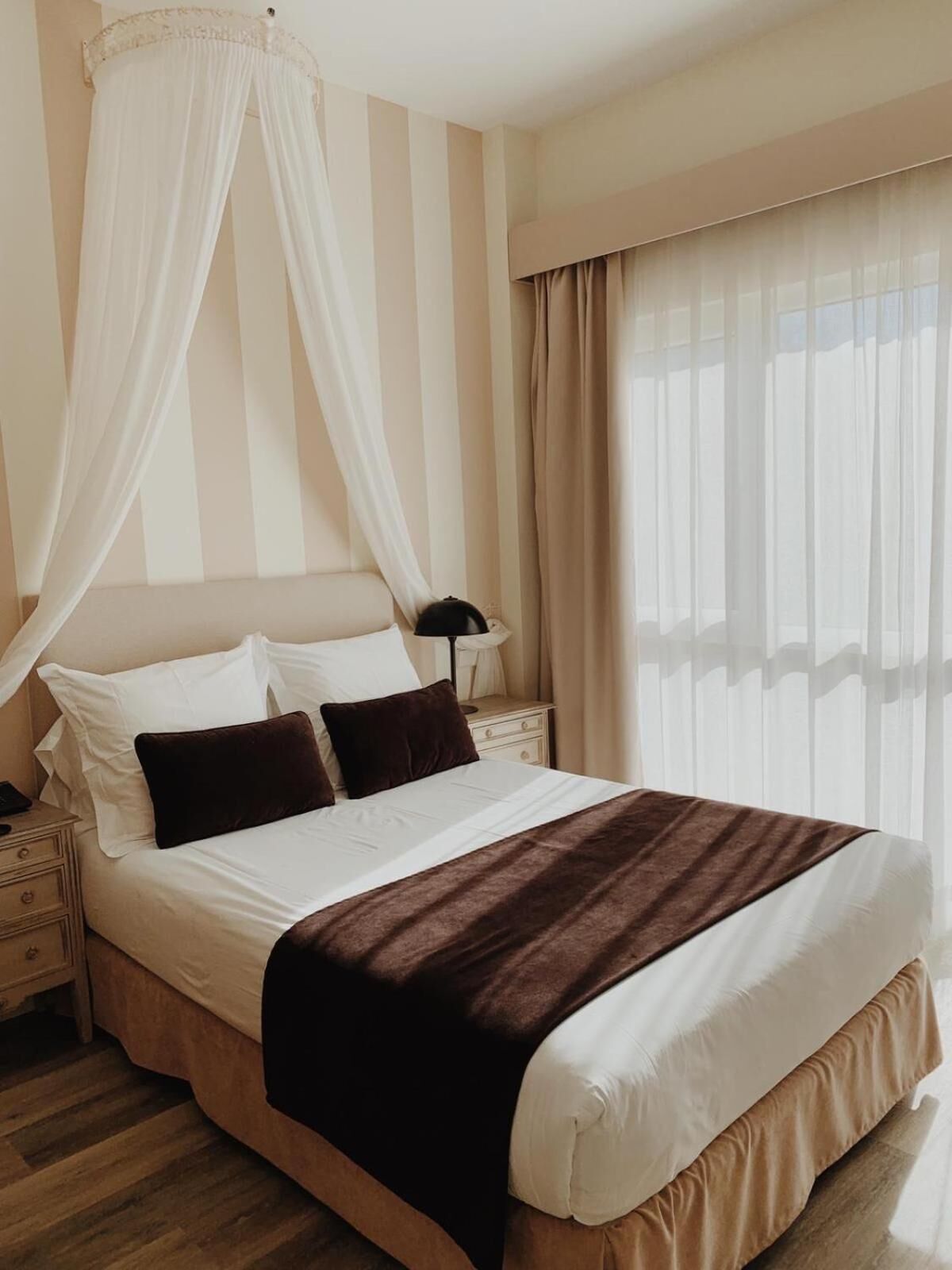 Una cama bien hecha con una manta marrón, una lámpara de noche y una mesita de noche.