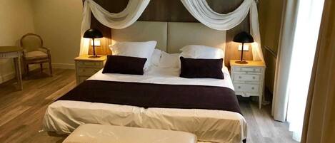 A neatly made bed with a canopy, two bedside tables with lamps, a chair, and a bench.