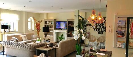 A modern living room with a sofa, coffee table, and decorative items. There is a television, a bookshelf, and a wall with motivational quotes.