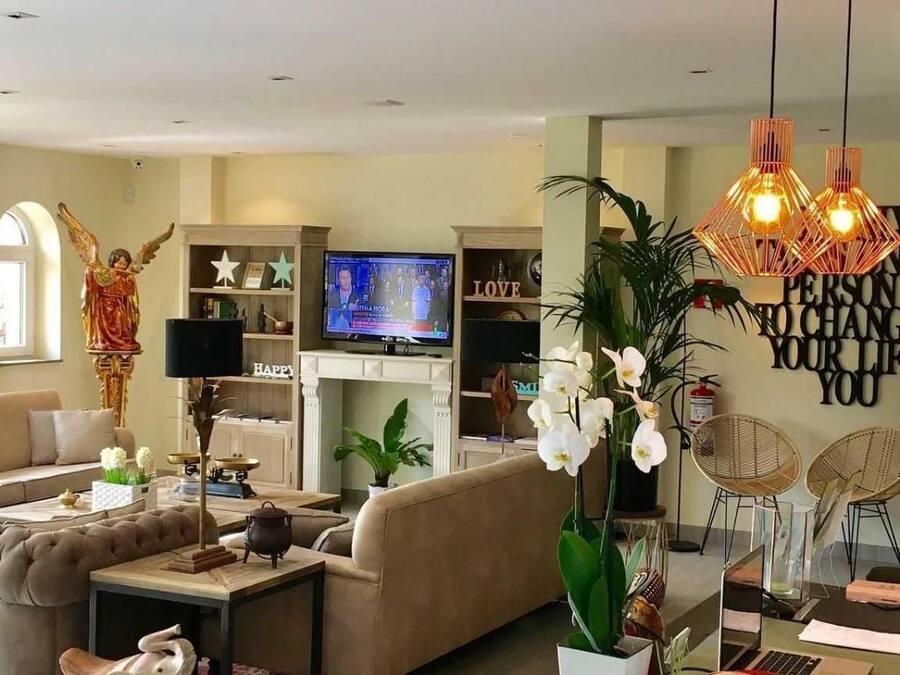 Una sala de estar moderna con sofá, mesa de centro y objetos decorativos. Hay un televisor, una estantería y una pared con citas motivacionales.