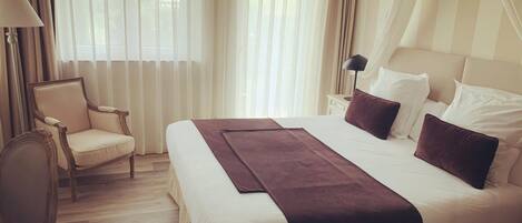 A hotel room with a large bed, a chair, a nightstand, and a window with curtains.