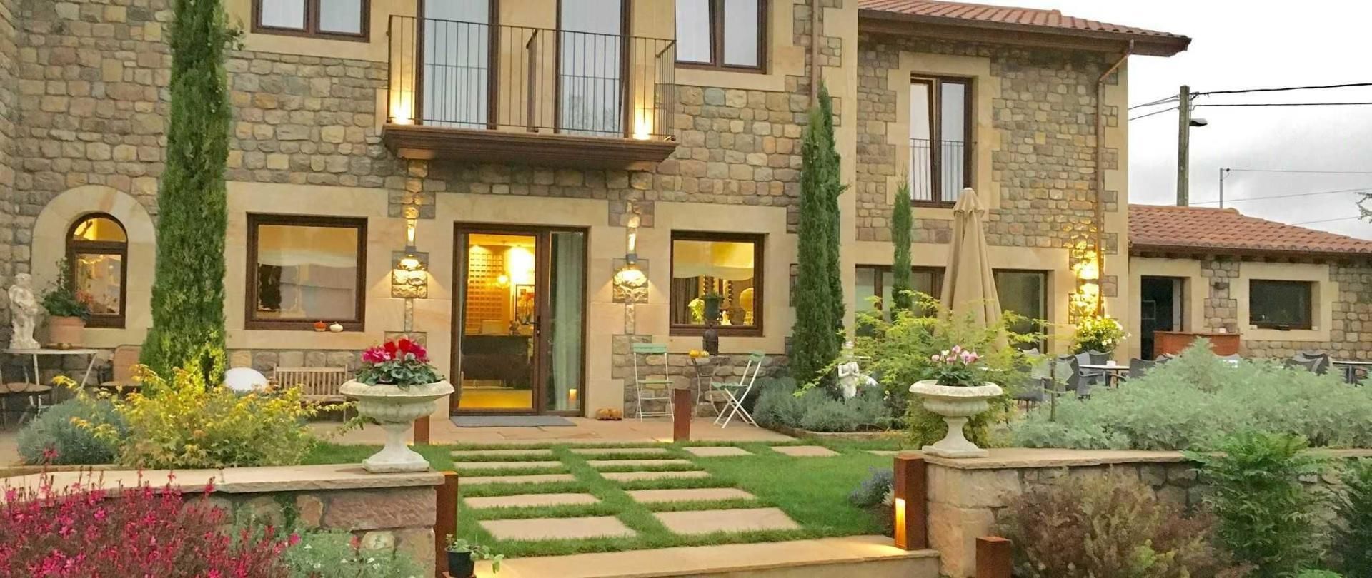 Un edificio de piedra con una entrada central, varias ventanas y zonas de estar al aire libre.