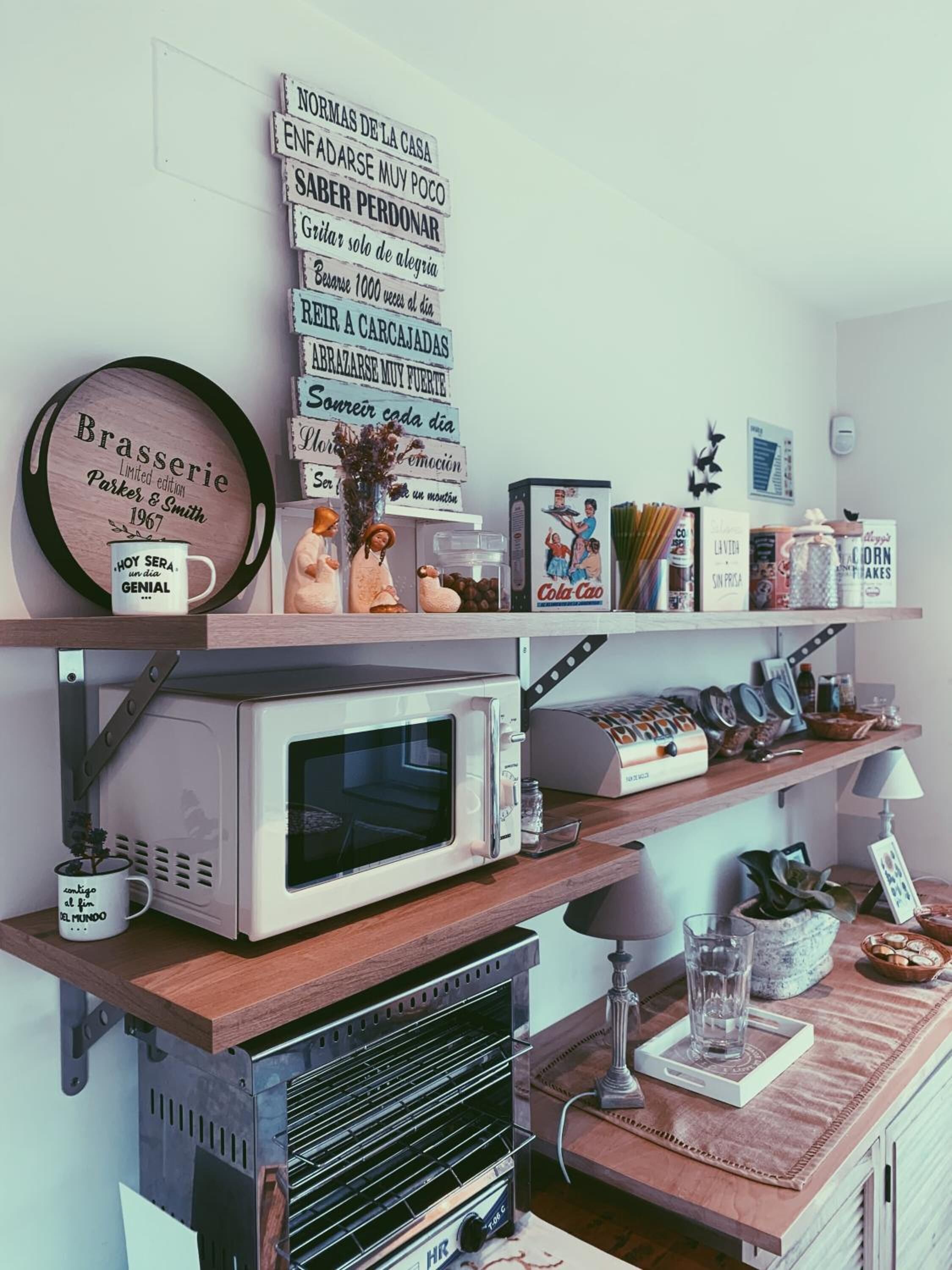 A kitchen with a microwave, toaster, and a shelf with various items including a coffee maker, books, and a decorative plate.