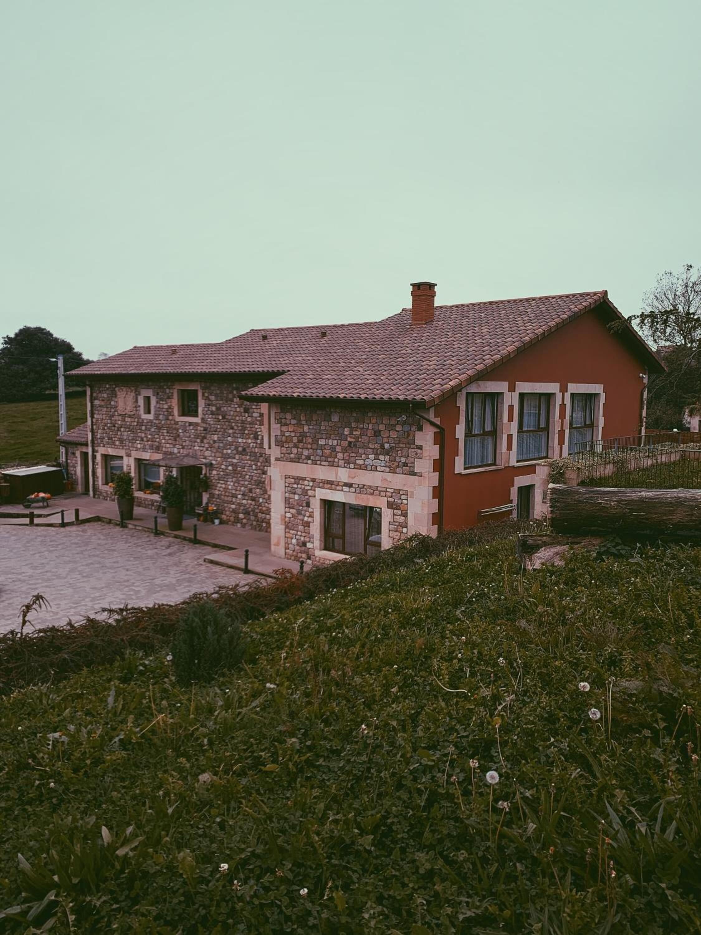 A two-story stone house with a red-tiled roof, a stone facade, and a paved driveway.