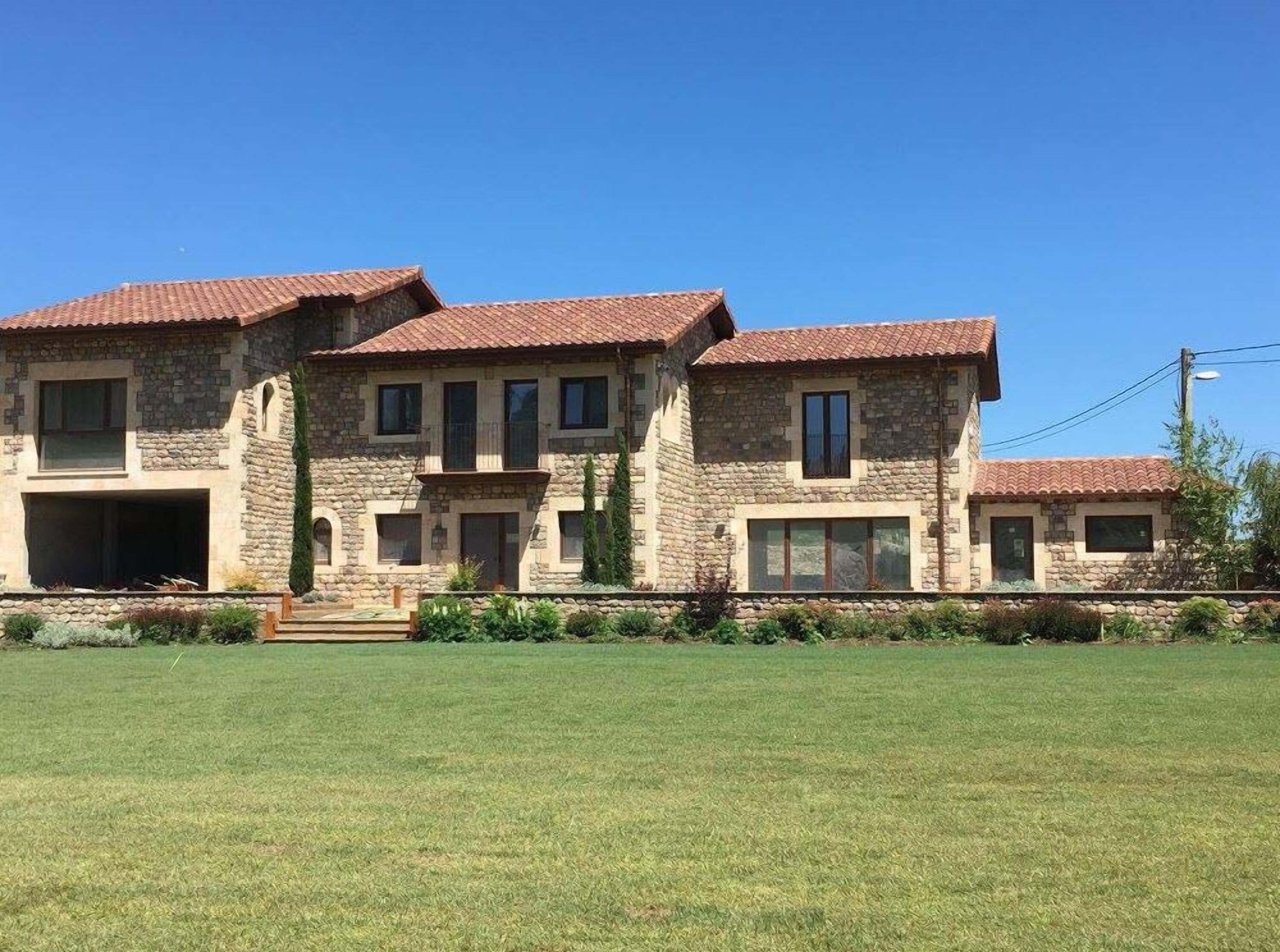 Une grande maison en pierre, avec un toit recouvert de tuiles rouges, de nombreuses fenêtres et une pelouse bien entretenue.