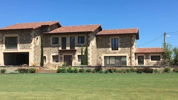 Une grande maison en pierre, avec un toit recouvert de tuiles rouges, de nombreuses fenêtres et une pelouse bien entretenue.