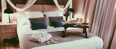 A bedroom with a bed, bedside tables, a nightstand, a bedside lamp, a tray with items, and a window with curtains.