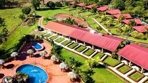 Eine Luftaufnahme eines Resorts mit einem langgezogenen Gebäude mit roten Dächern, einem Swimmingpool und gepflegten Gärten.