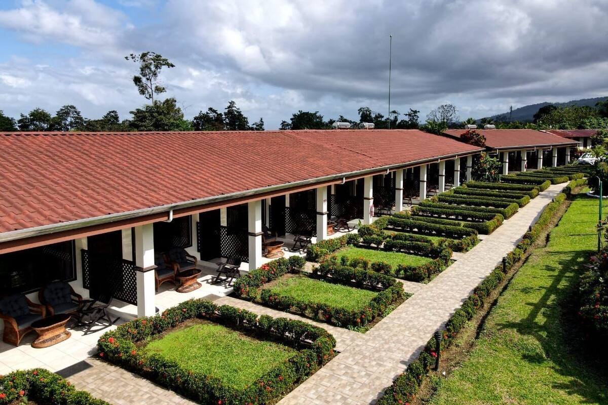 Un hotel con una zona salotto esterna coperta, giardini curati e un tetto in tegole rosse.