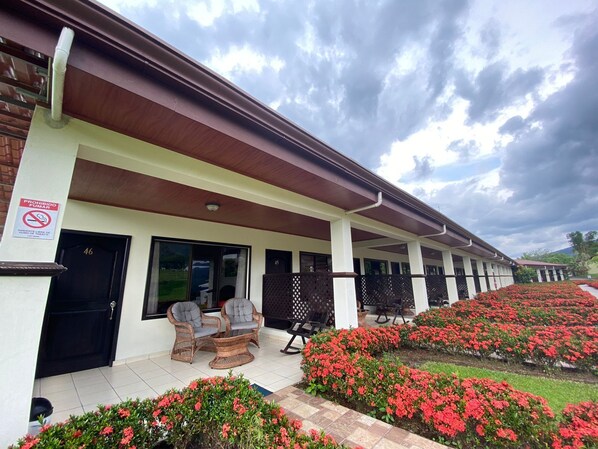 Un hotel con un área de estar al aire libre cubierta, un letrero que prohíbe fumar y una hilera de habitaciones con números en las puertas.