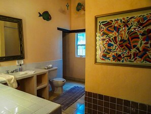 Ein Badezimmer mit weißem Waschbecken, Toilette, Spiegel und einem farbenfrohen, abstrakten Gemälde an der Wand.