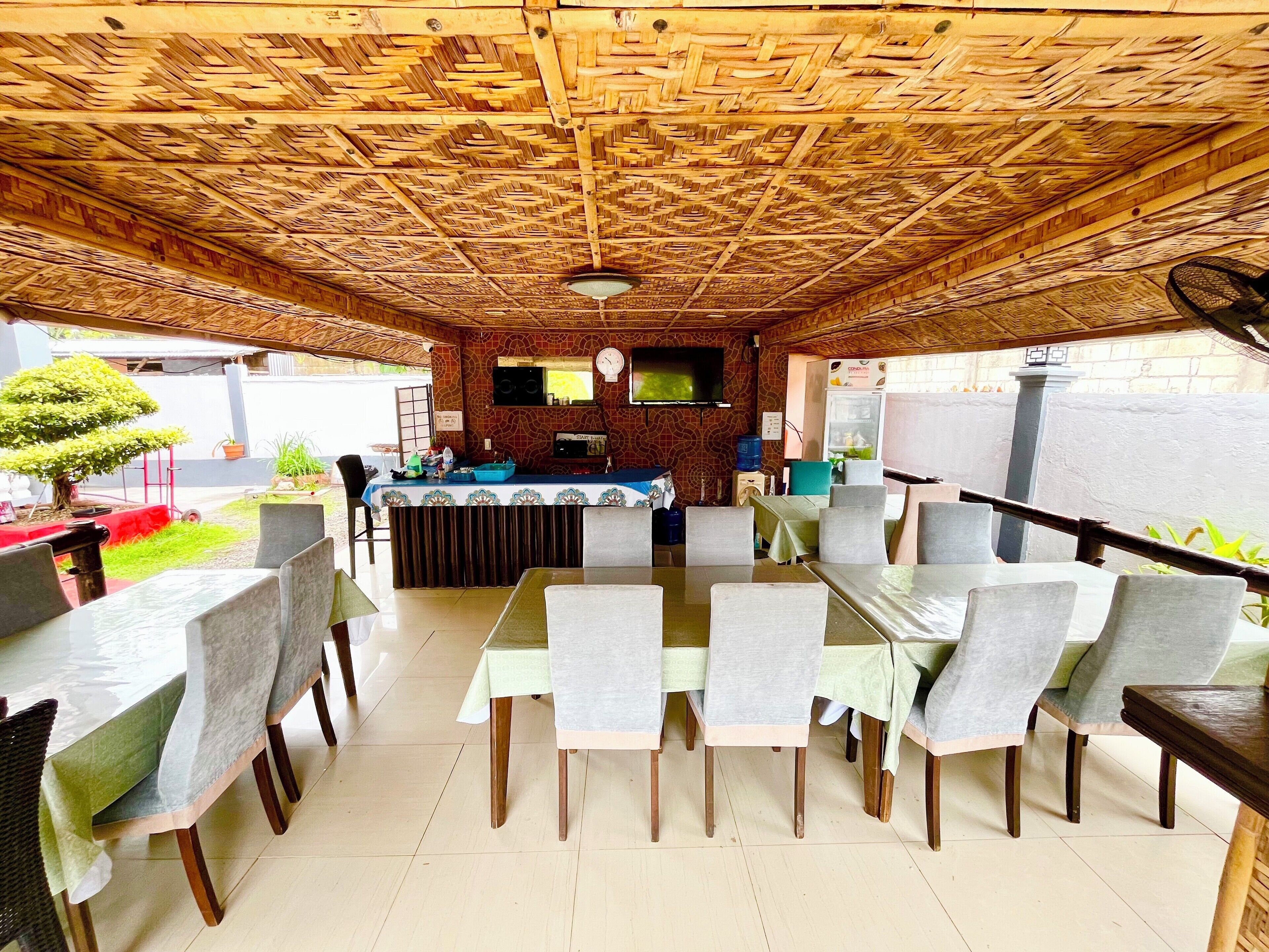 An outdoor dining area with a bamboo ceiling, a bar counter, and several tables and chairs.