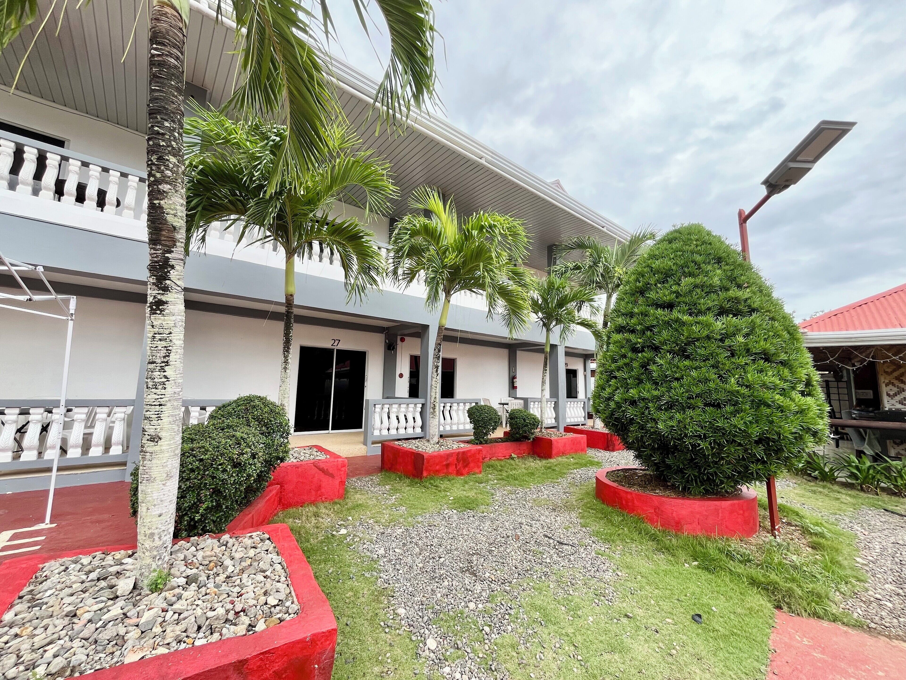 A hotel courtyard with palm trees, red planters, and a building with a balcony.