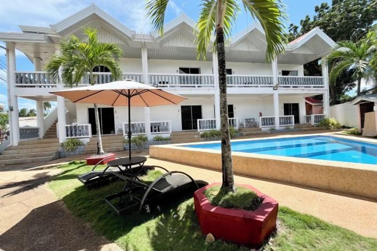 Um edifício de dois andares com piscina, área de estar externa e palmeiras.
