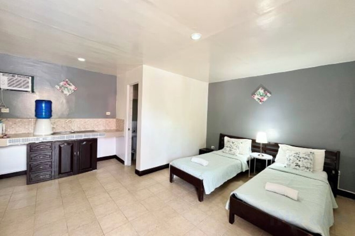 A hotel room with two beds, a kitchenette, and a bathroom.