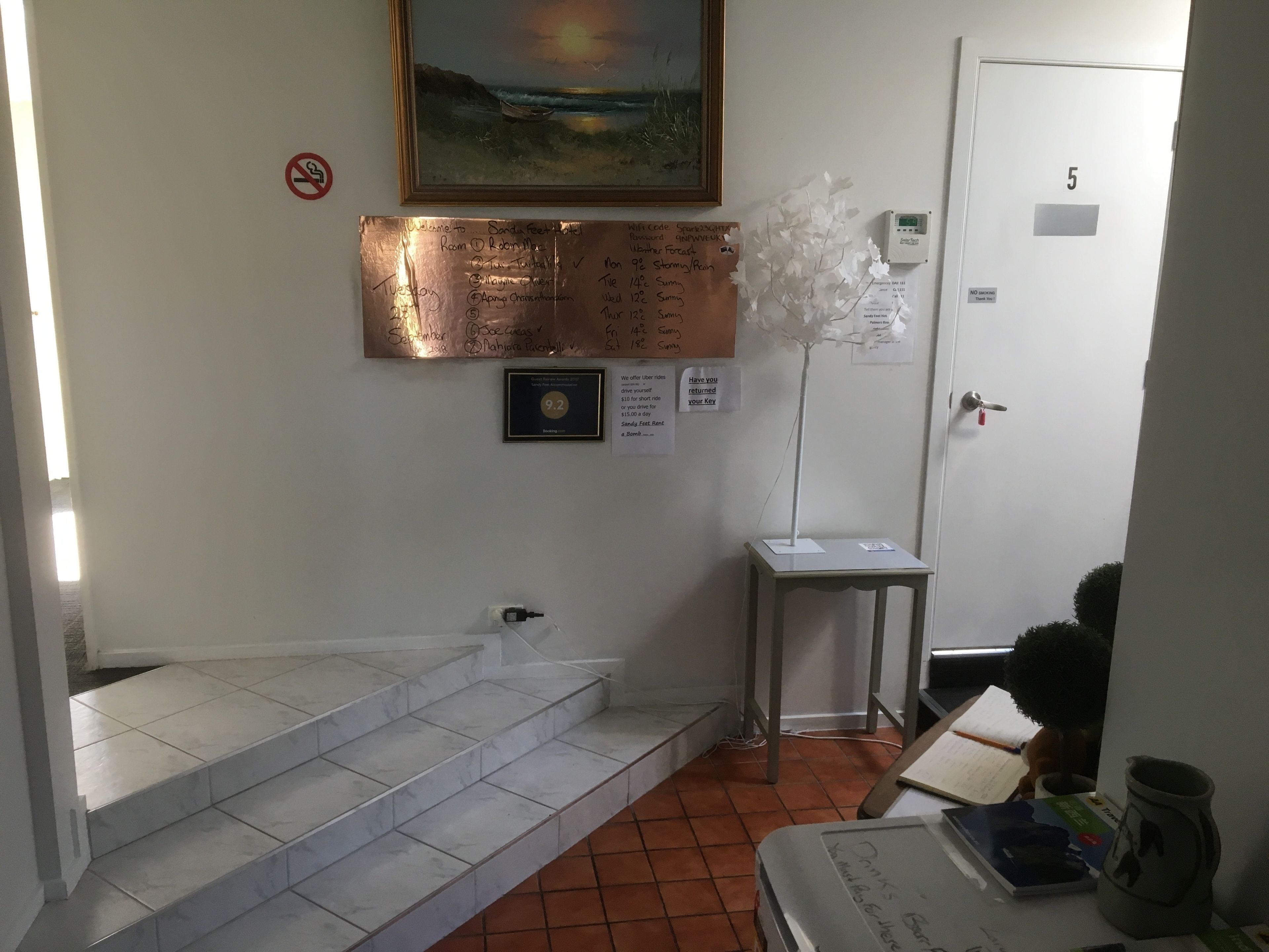 A hotel reception area with a painting, a bronze plaque, a framed certificate, and a flower arrangement on a table.