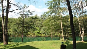 Ein friedliches Außenareal mit Teich, umgeben von Bäumen und einer Rasenfläche mit einem Holzpfosten.