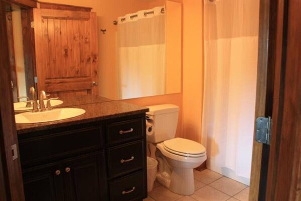 A bathroom with a wooden vanity, a toilet, and a shower curtain.