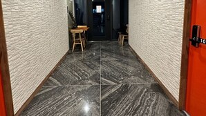 A hallway with a modern design, featuring a marble floor and brick-patterned walls. There is a wooden table and chairs in the center, and a red door on the right. - Insadong R Guesthouse (Seoul)