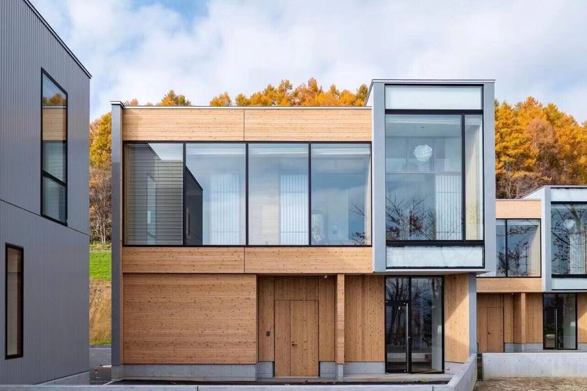 En modern byggnad med stora fönster, en träfasad och ett platt tak.