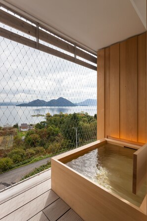 A wooden hot tub on a balcony with a view of a body of water and mountains. - WE Hotel Toya - Dusit Collection (Toyako)
