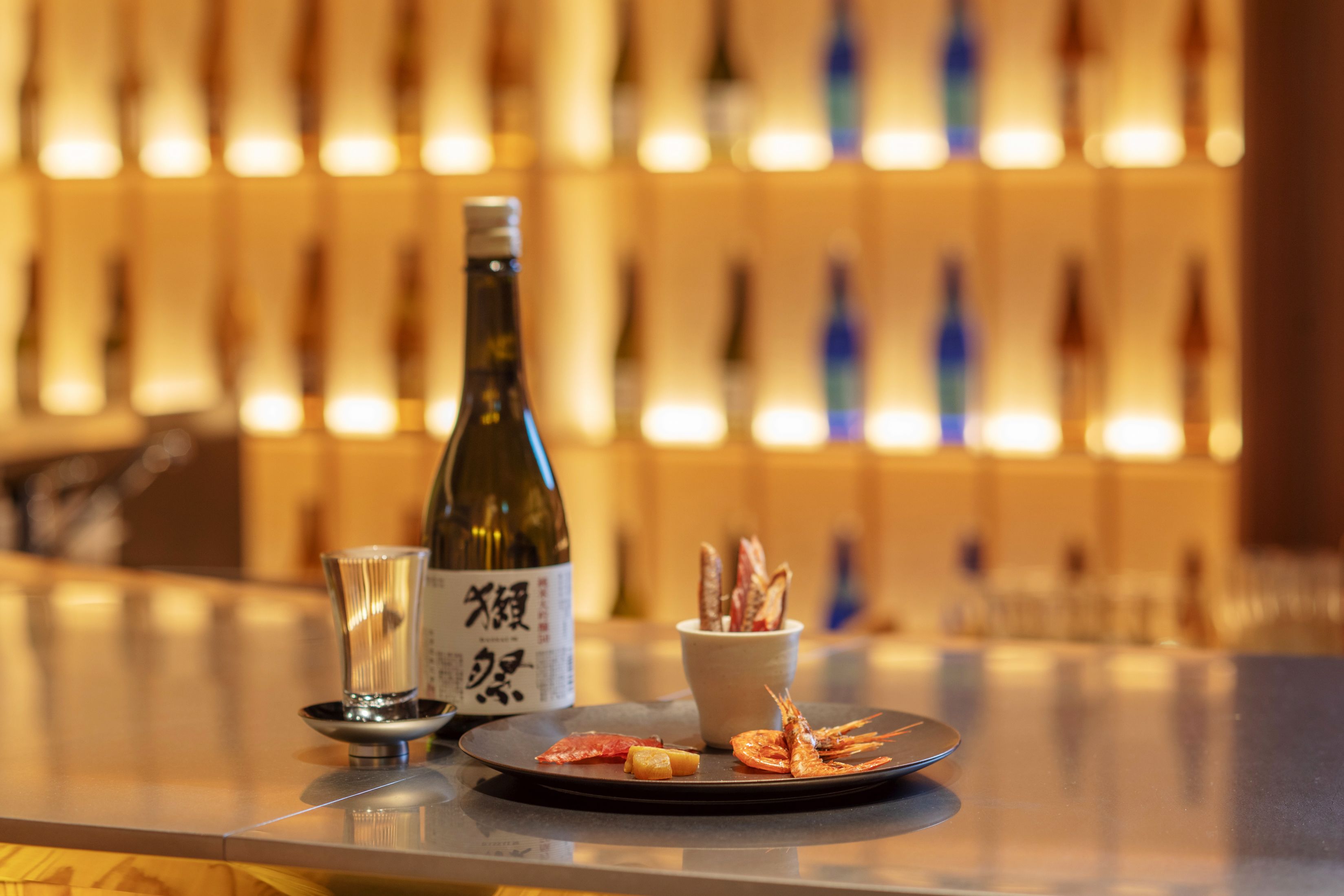 A bar setting with a bottle of wine, a glass, and a plate with food.