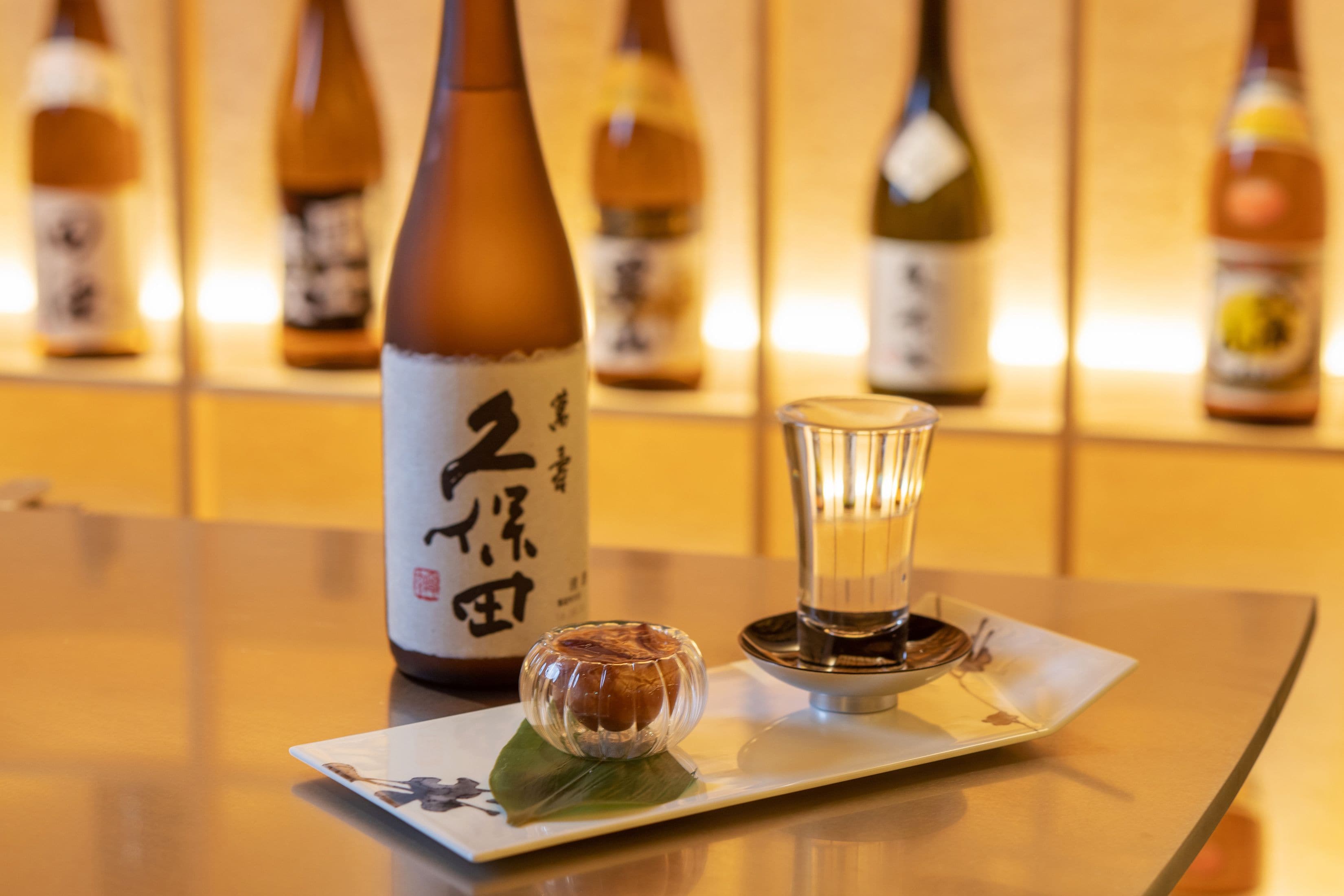 A table with a bottle of sake, a sake cup, and a small dish with a leaf.