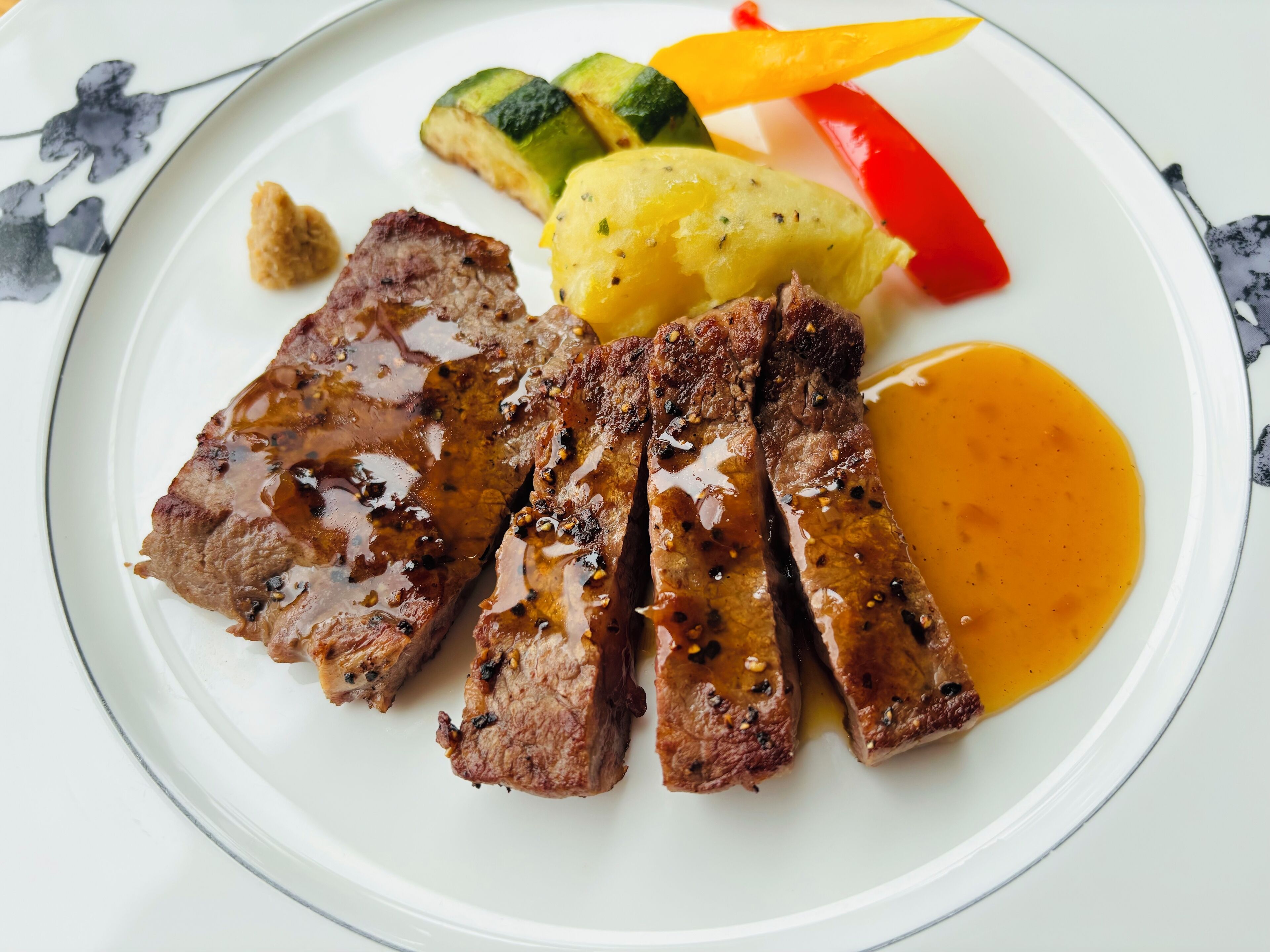 A plate with sliced meat, mashed potatoes, and grilled vegetables.