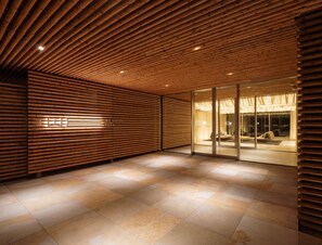 A hotel lobby with wooden slatted ceilings, a glass partition, and a tiled floor. - WE Hotel Toya - Dusit Collection (Toyako)