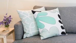 Ein modernes Wohnzimmer mit einem grauen Sofa, einem weißen Beistelltisch mit einer Vase voller violetter Blumen und einer weißen Stehlampe.