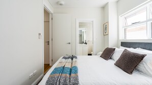 Ein modernes Schlafzimmer mit einem großen Bett, einem Nachttisch, einem Spiegel und einem Fenster.