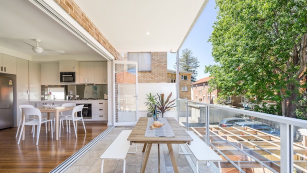 Eine moderne Küche mit weißen Schränken, einem Holztisch und Blick auf die Stadt durch große Fenster.